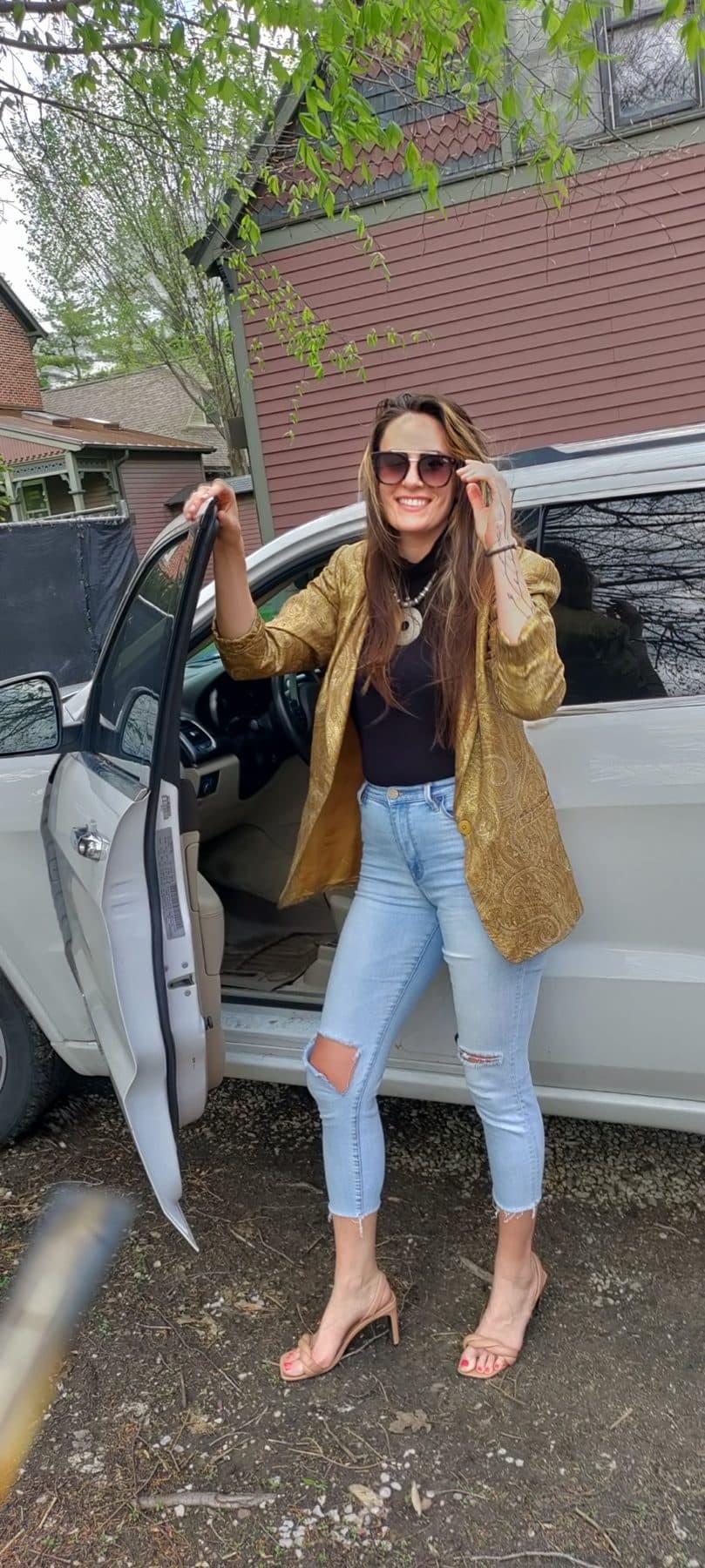 Leaning on the open door of a white Jeep, tan blazer and distressed denim.