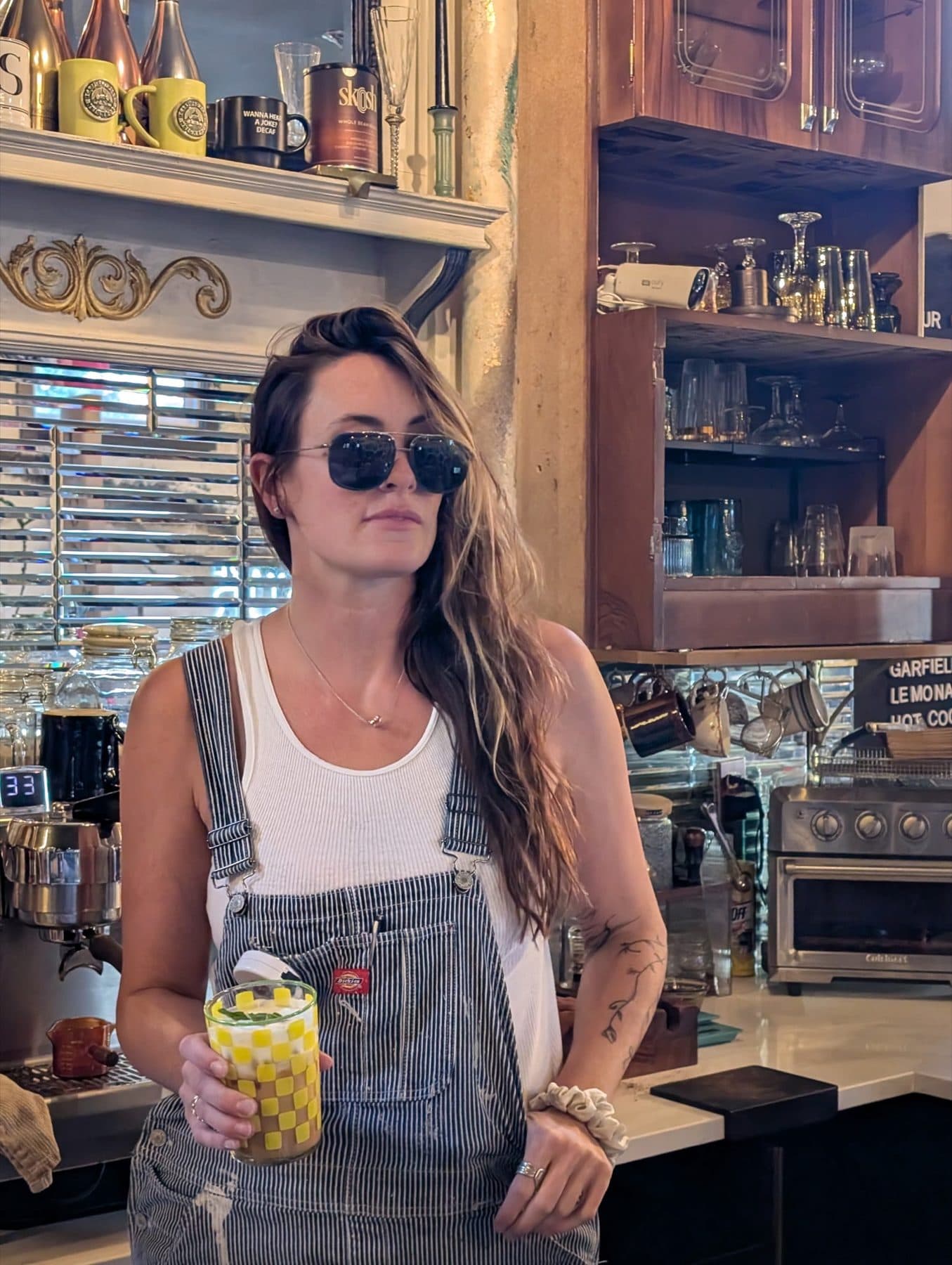 Denim overalls and a white tank in a coffee shop, sunglasses on.