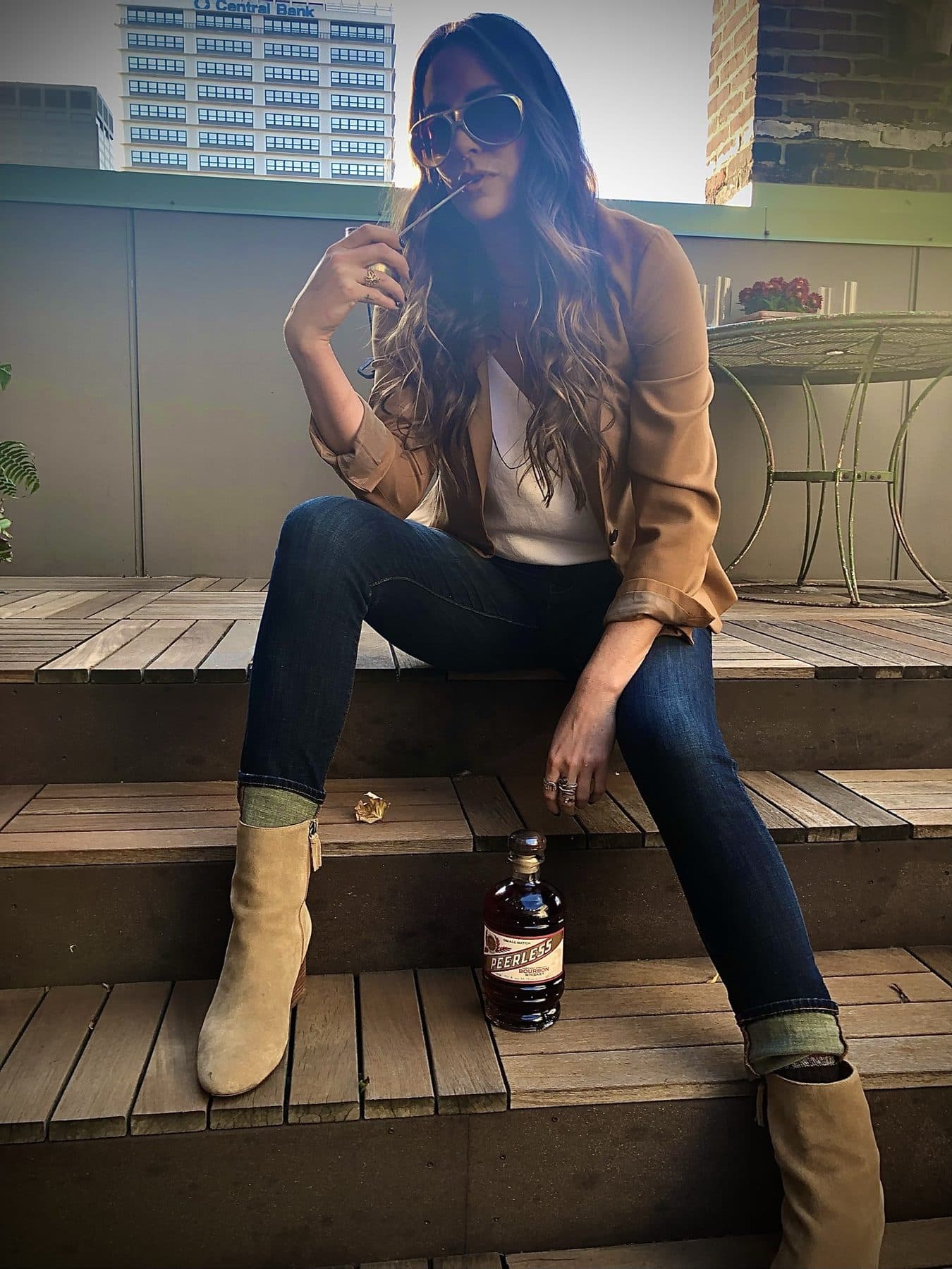 Sitting on wooden steps in a tan blouse, denim, and suede boots.