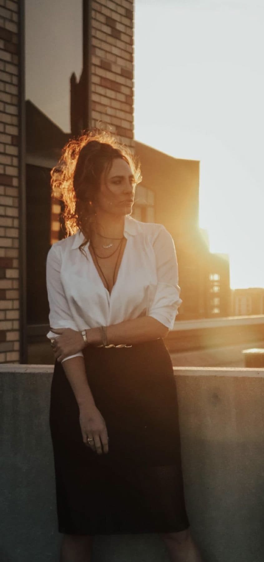 Golden-hour portrait in a white blouse, curls backlit by the sun.