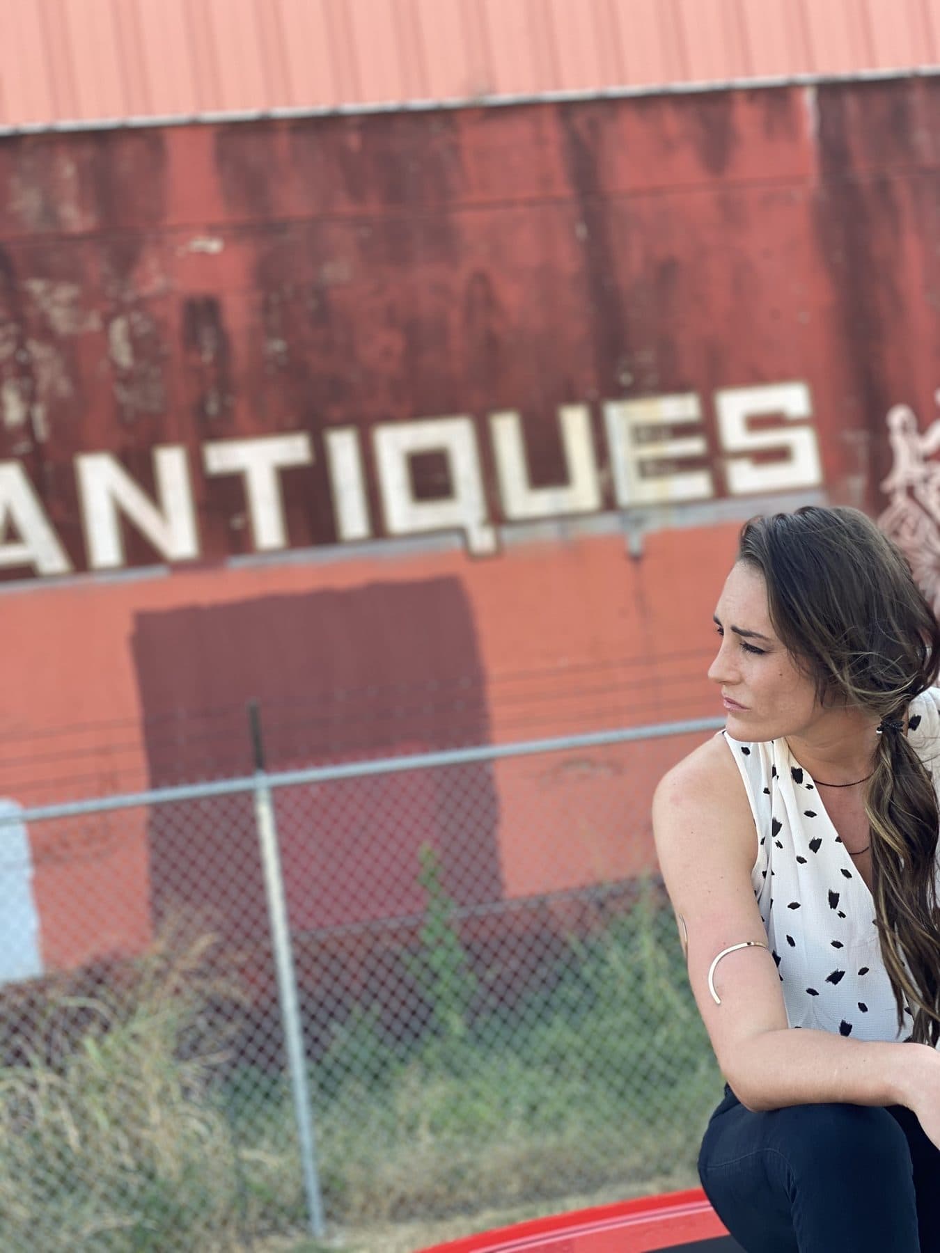 Looking over one shoulder in front of a red ANTIQUES sign.