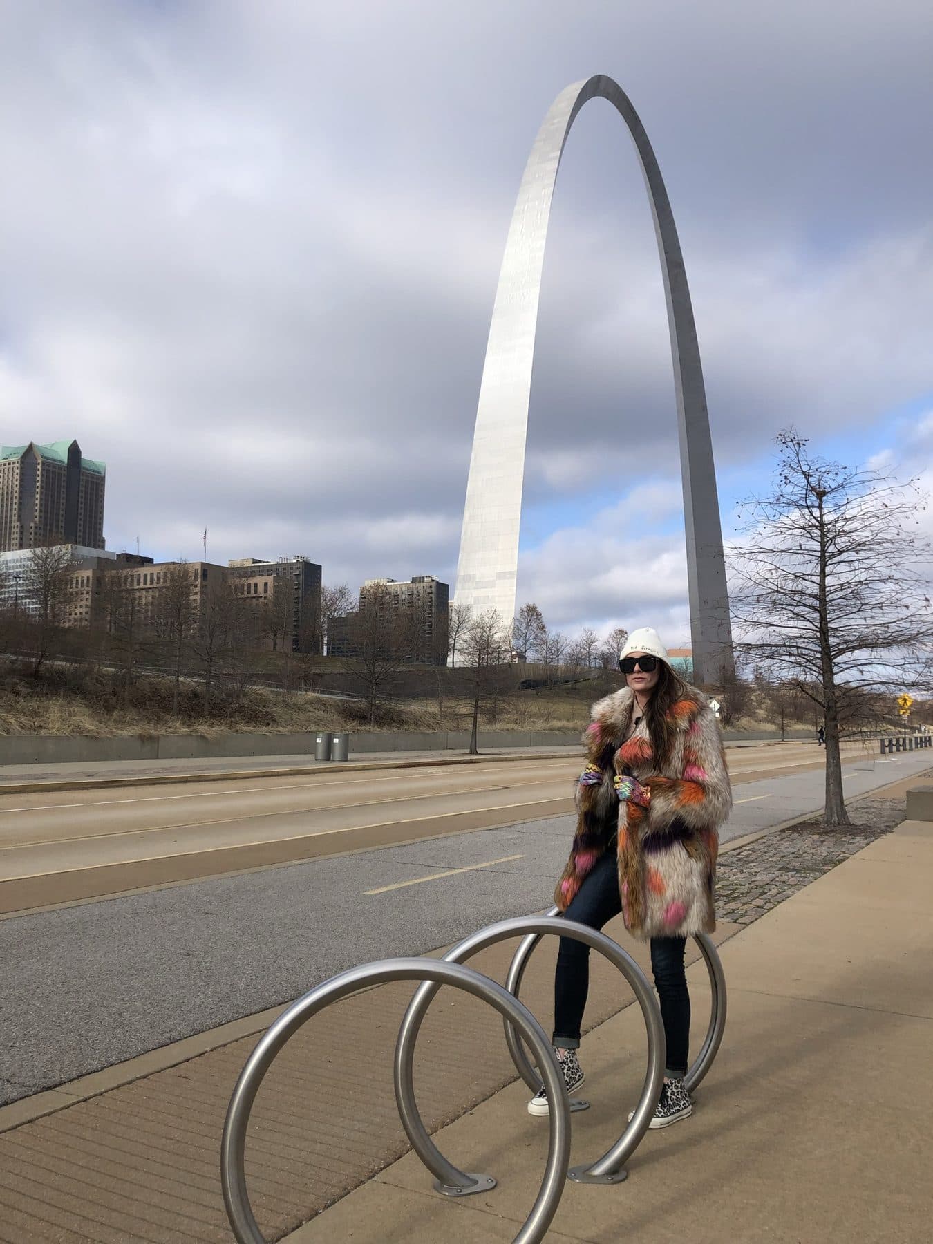 Under a stainless-steel arch sculpture, arms wide.
