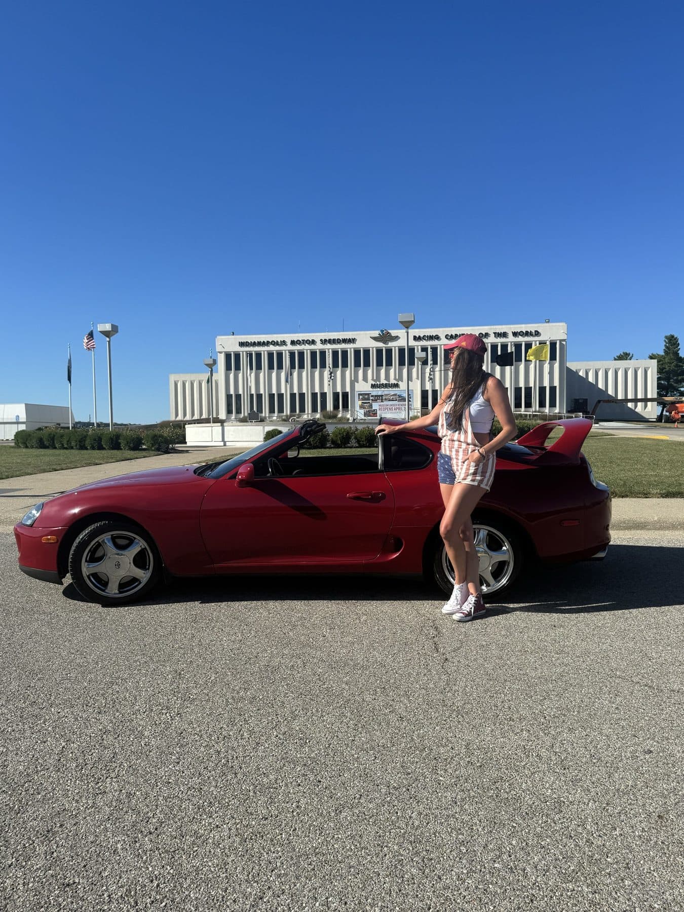 Beside a red vintage convertible on a blue-sky street.