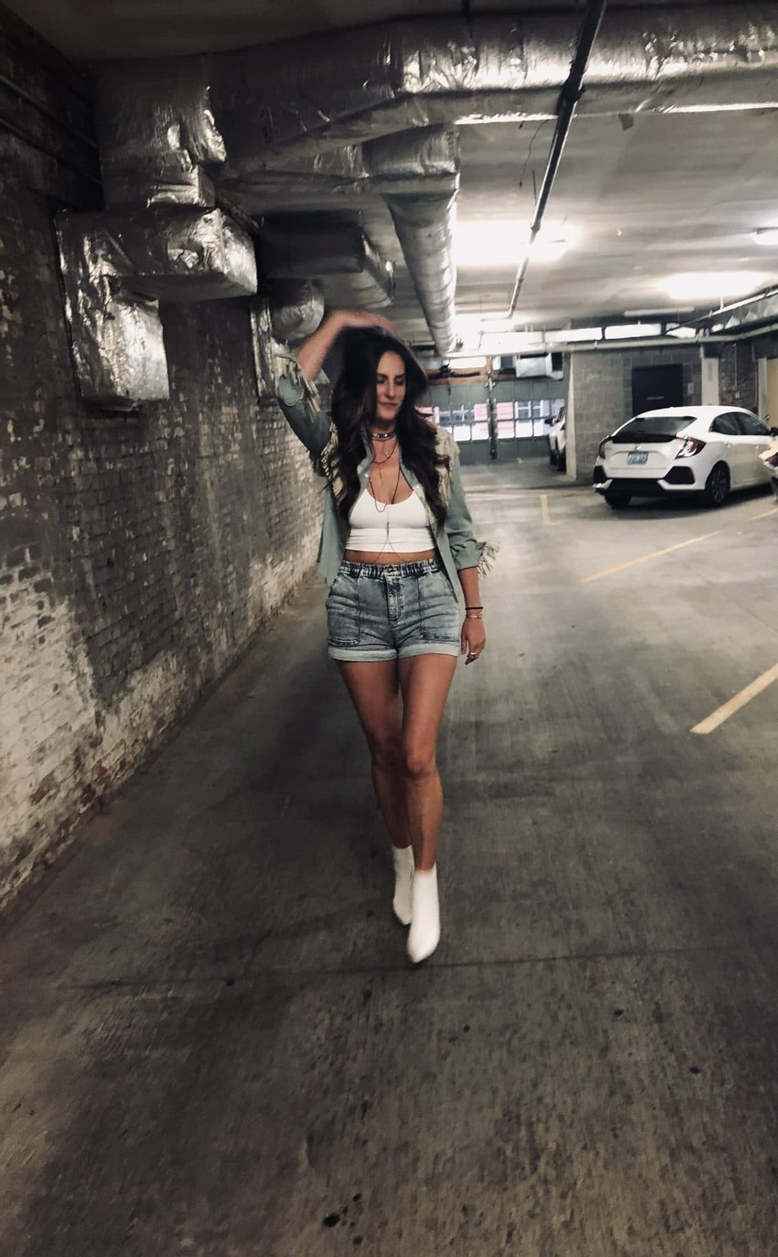 Walking through a parking garage in white boots and denim shorts.