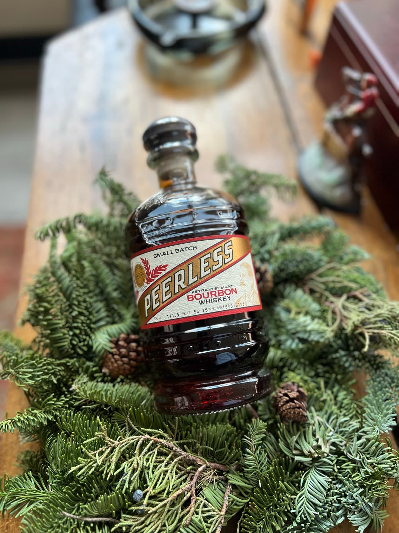 A bourbon bottle nestled in evergreen, low and moody.