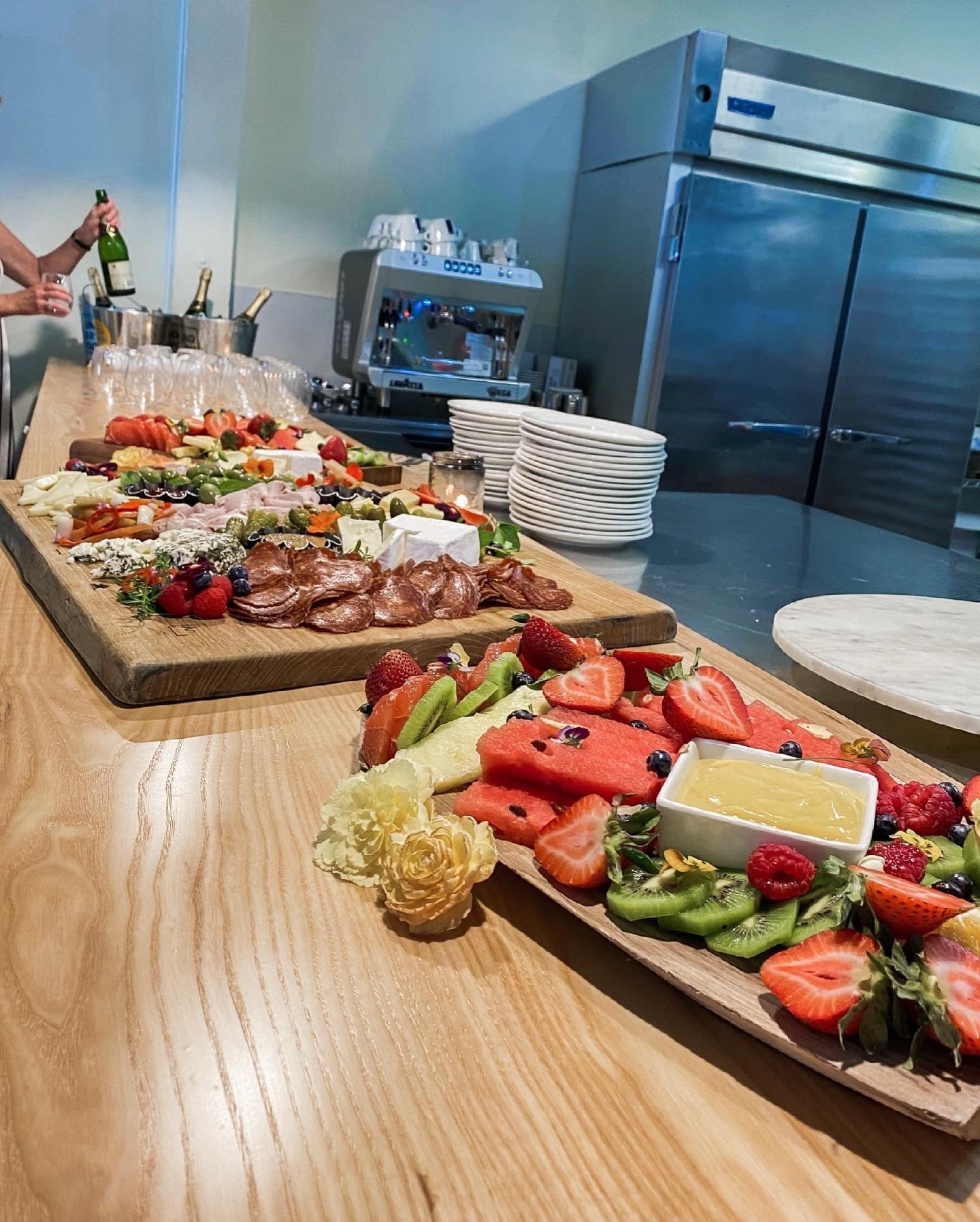 Layered charcuterie and fresh-fruit boards on a live-edge bar with champagne chilling and stemware lined up behind.