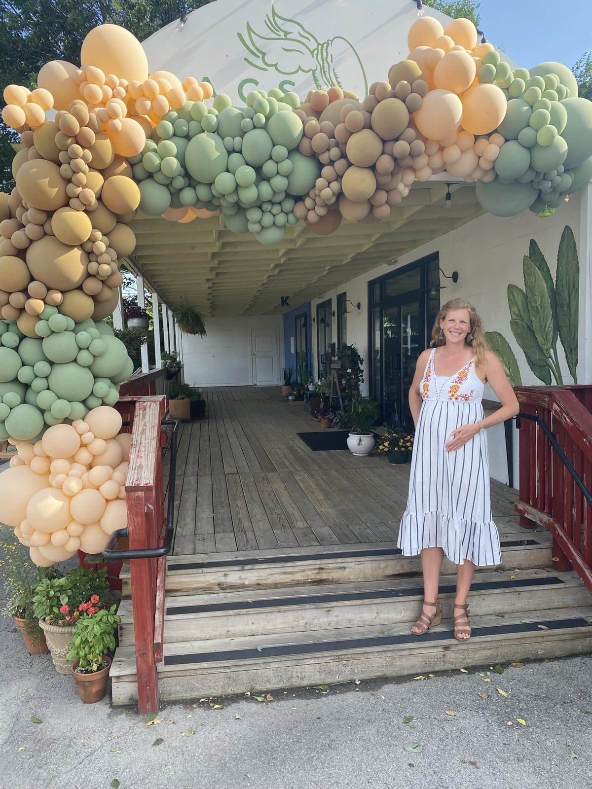 The mom-to-be on the pastry shop's front steps beneath the entrance balloon arch.