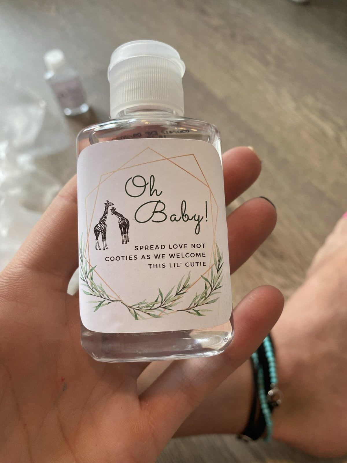 The 'Oh Baby! Spread love, not cooties' sanitizer favor with giraffe line art, held up to the light.