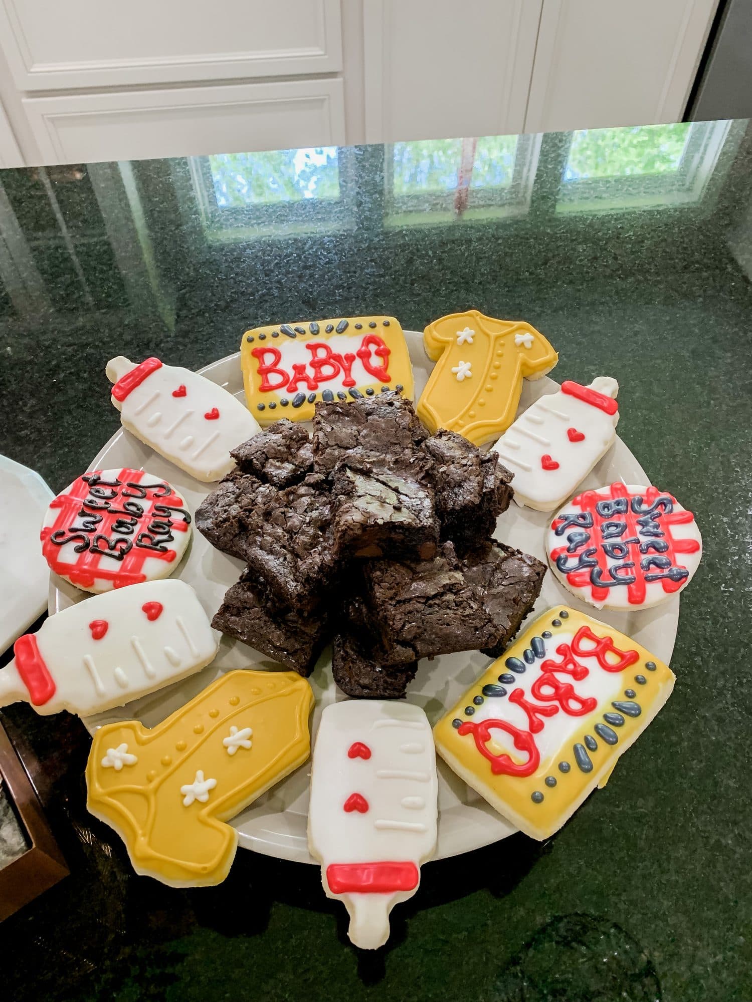 Hand-iced sugar cookies shaped as baby bottles and onesies reading 'Sweet Baby Ray' arranged around brownies on a white platter.