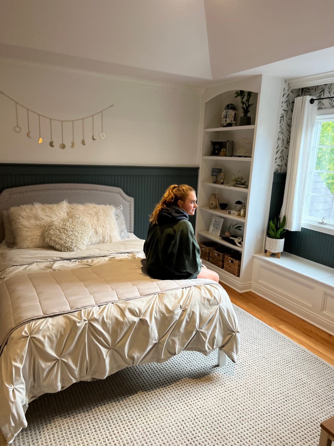 The teen perched on the end of the bed, the green beadboard headboard wall and the styled built-ins behind her.