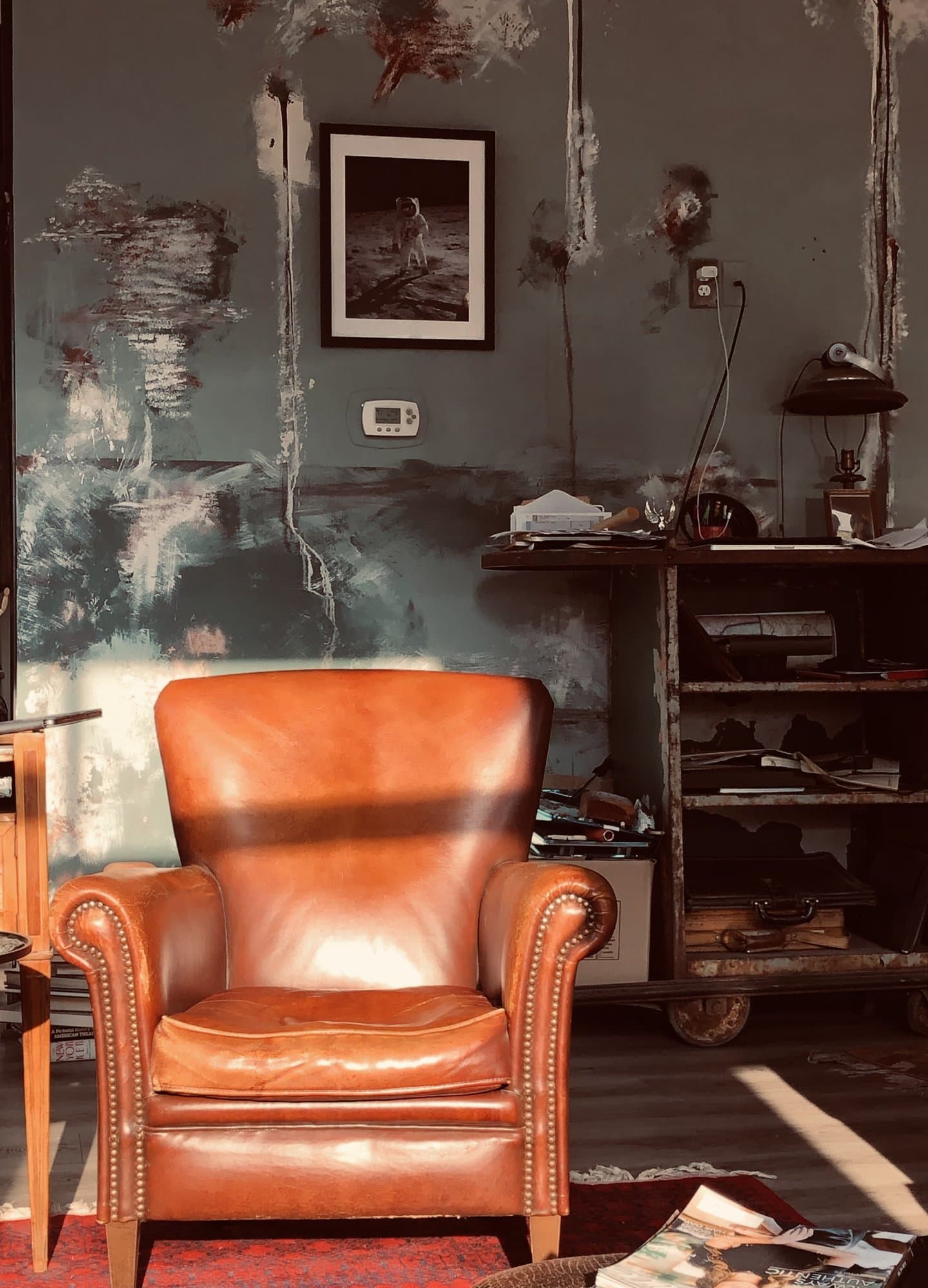 A cognac leather club chair and a framed moonwalk print set against the storm-teal plaster wall.