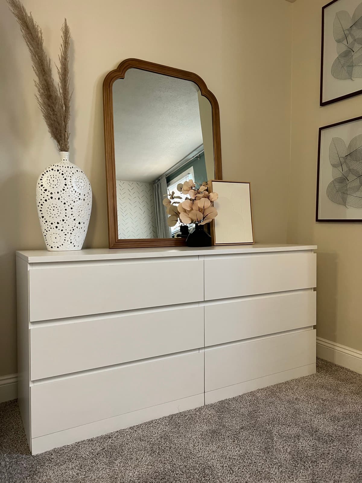Styled dresser vignette, white drawers, arched wood mirror, pampas grass, and botanical prints.