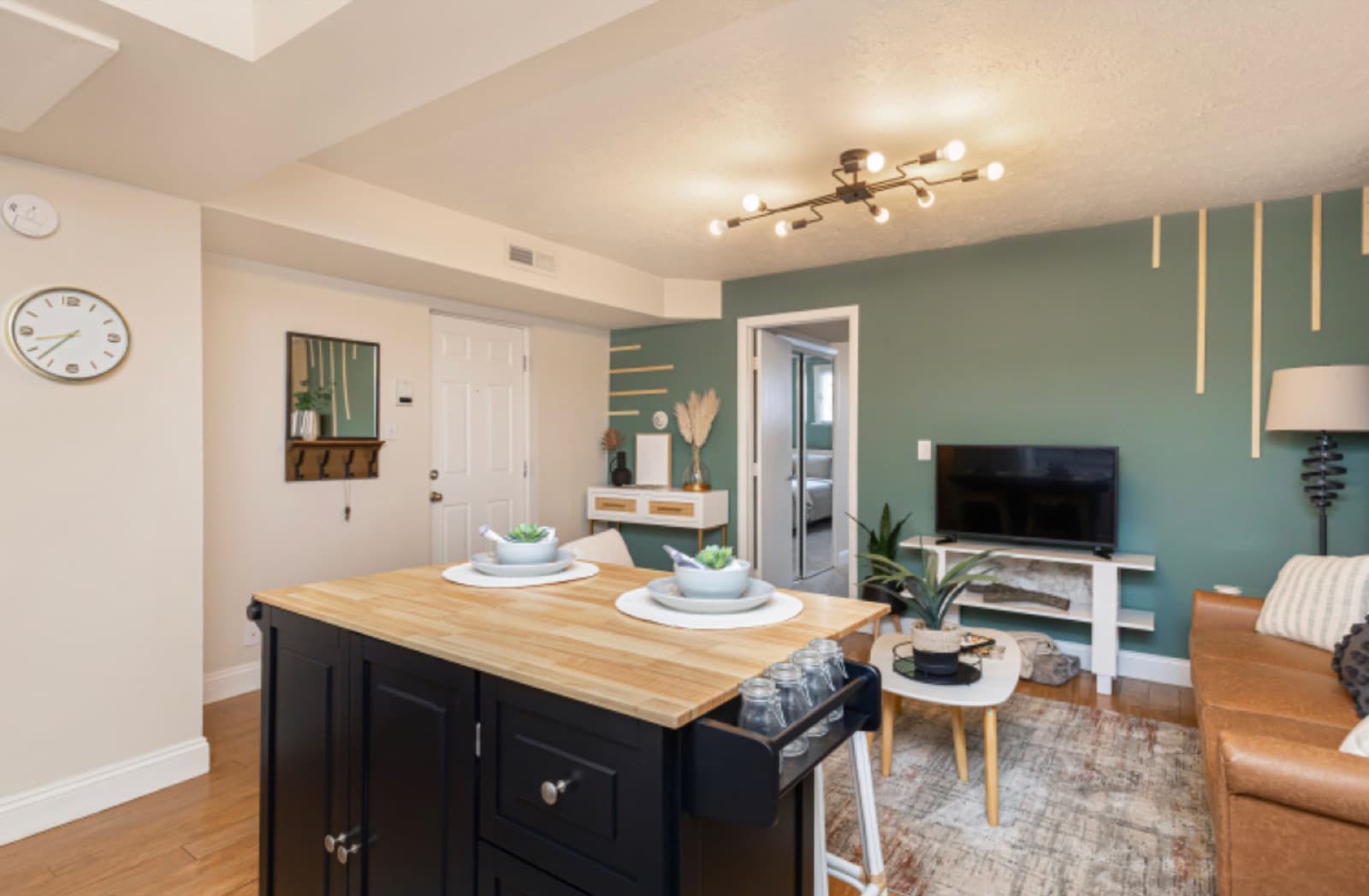 Open kitchen and living view, black butcher-block island set for two against the green accent wall.