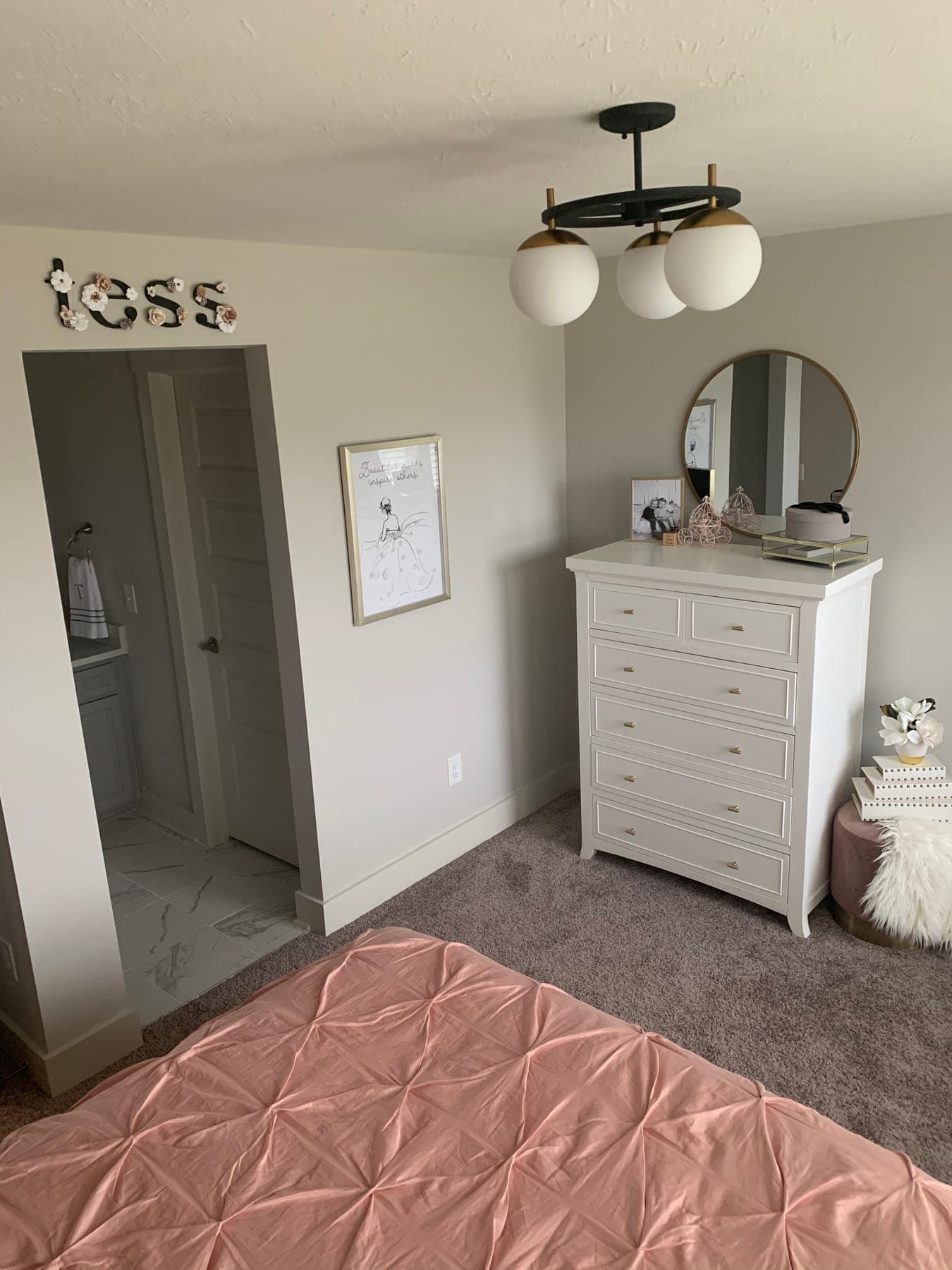 A white dresser beneath a brass round mirror, a framed print, and a faux-fur stool in the corner.