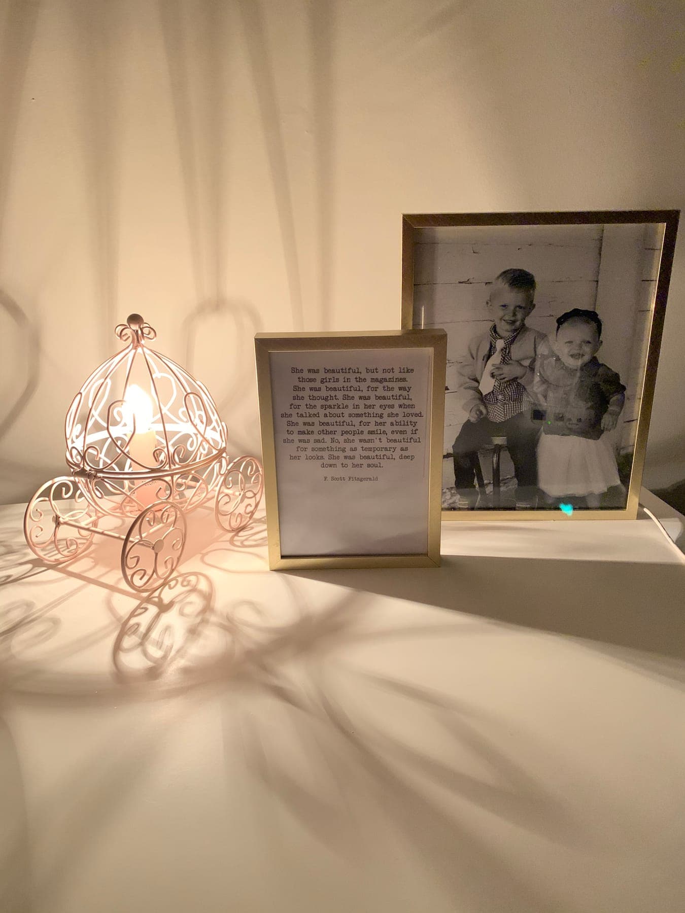 A wire pumpkin-carriage lamp throwing lace shadows beside a framed quote and a childhood photo.