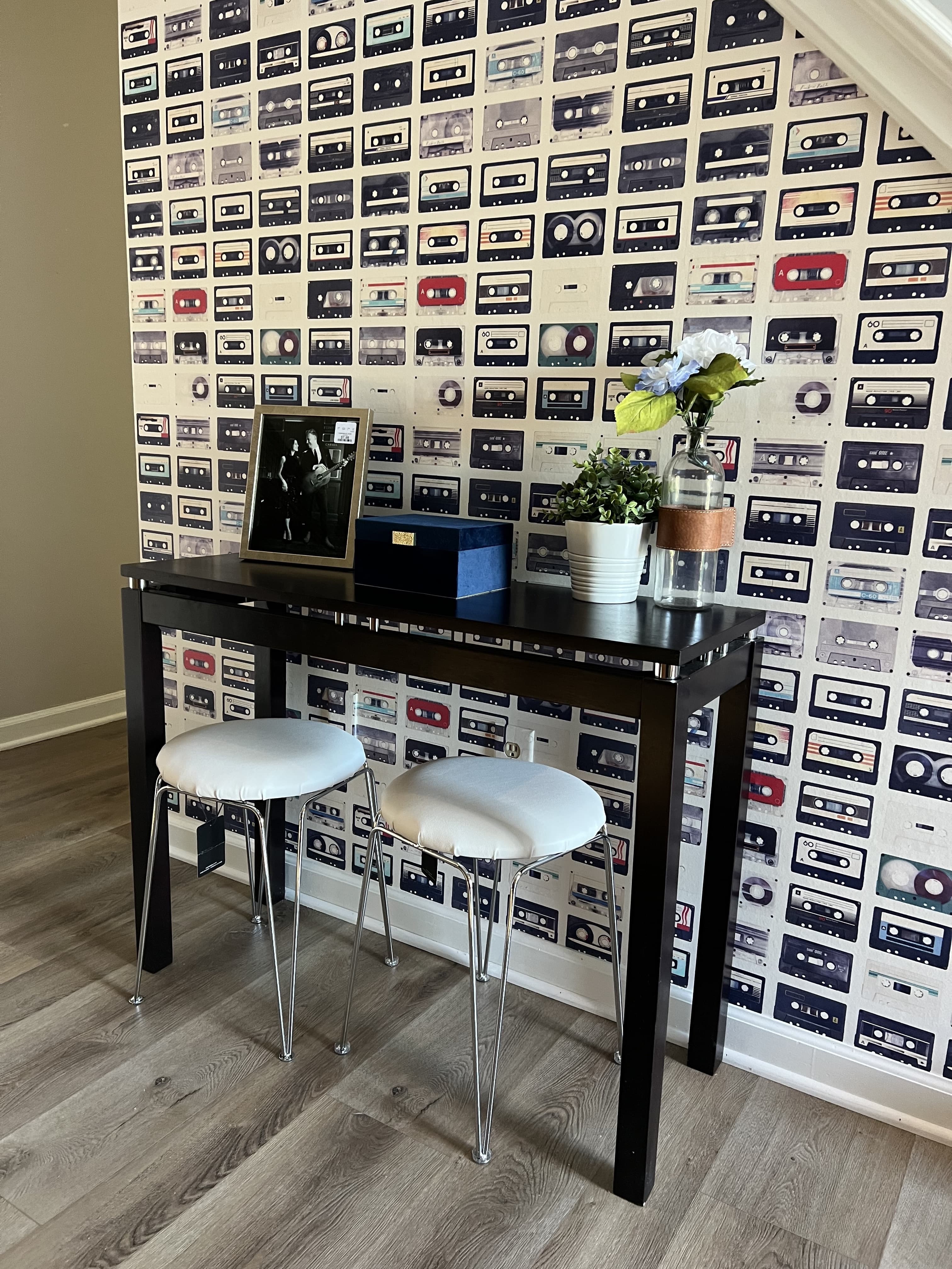 A cassette-print accent wall behind a slim bar table and two stools.