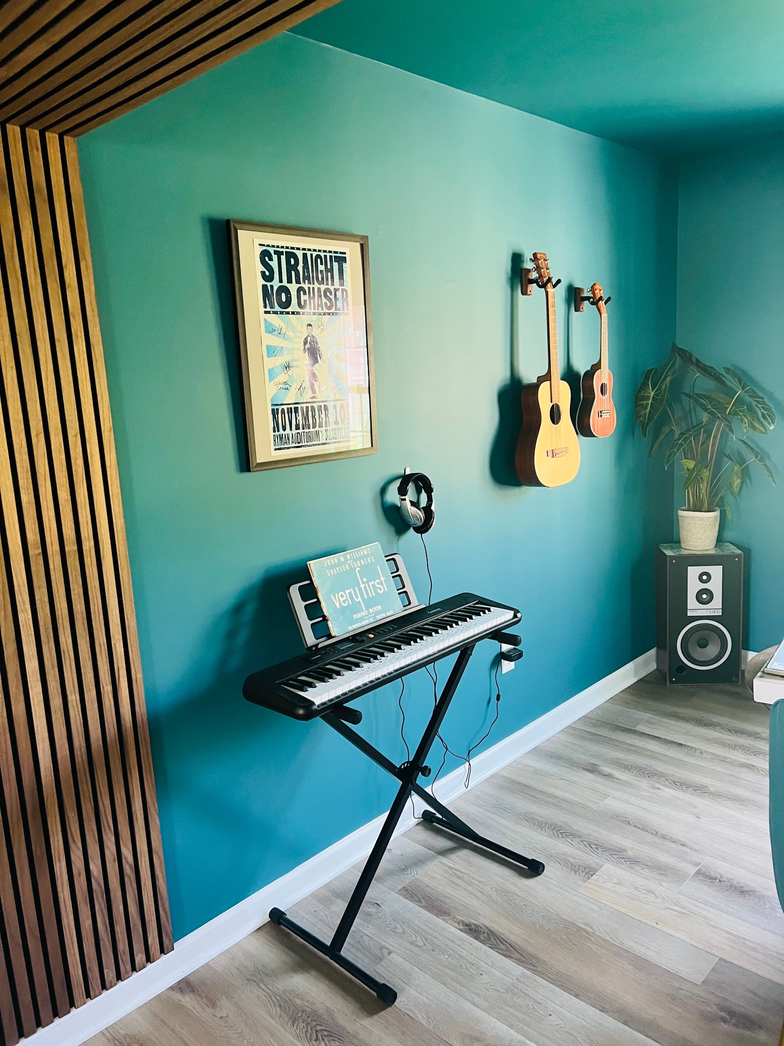 The music studio's teal wall, wall-mounted guitars, and keyboard stand.
