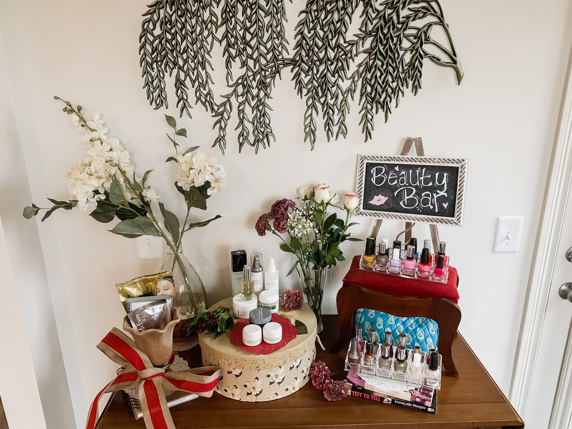 A 'Beauty Bar' station with nail polishes, face masks, and skincare arranged with white florals beneath a trailing greenery wall.
