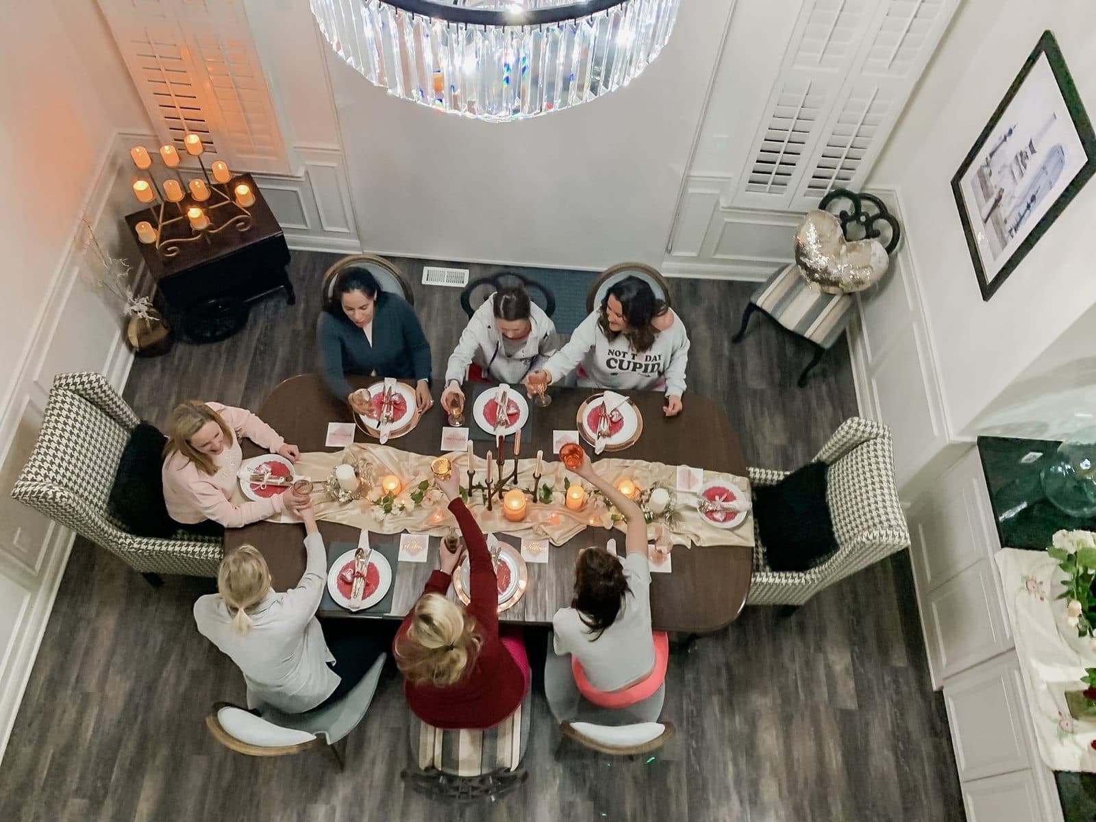The gals at the table, seen from the balcony: heart place settings, candles down the runner, everyone mid-conversation.
