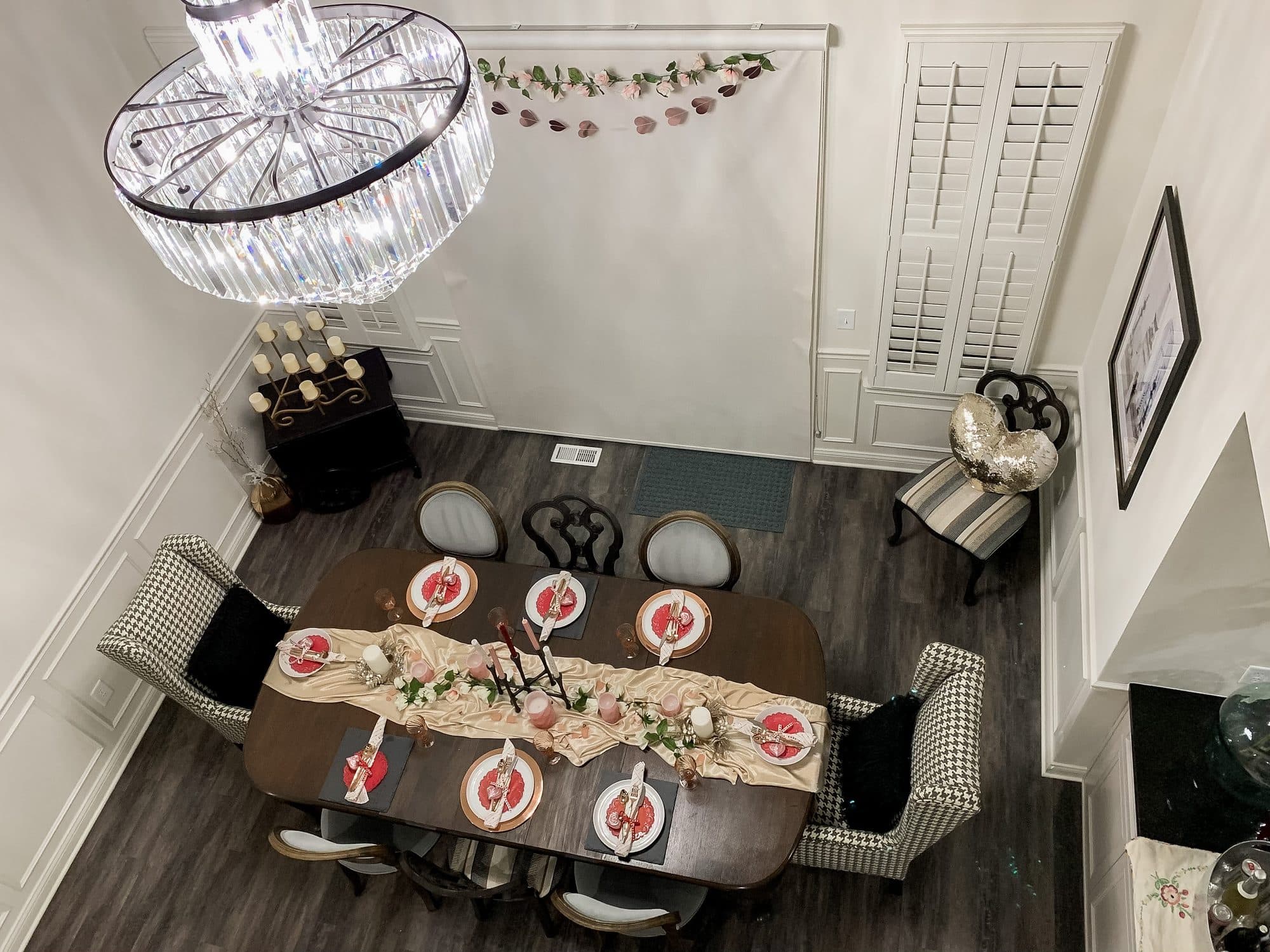 An overhead view of the dining table, heart chargers, blush runner, and candle line running its length in the double-height room.
