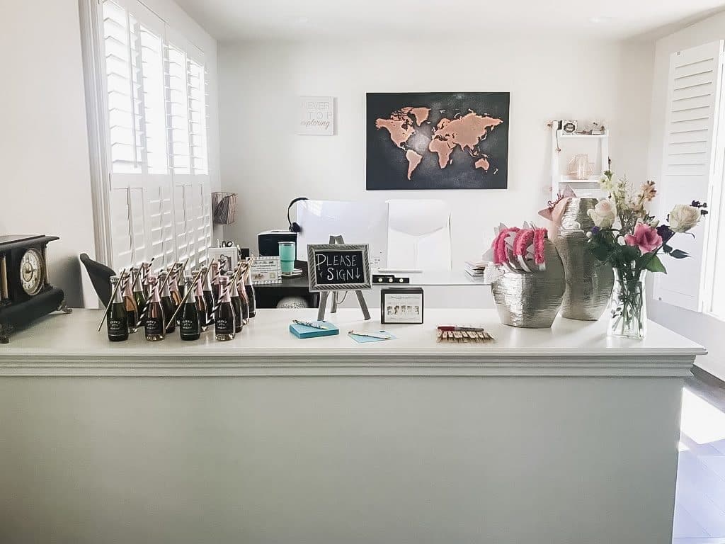 A guestbook table with a copper-and-black world-map canvas, a 'Please Sign' chalk easel, rosé favors, and blush florals.