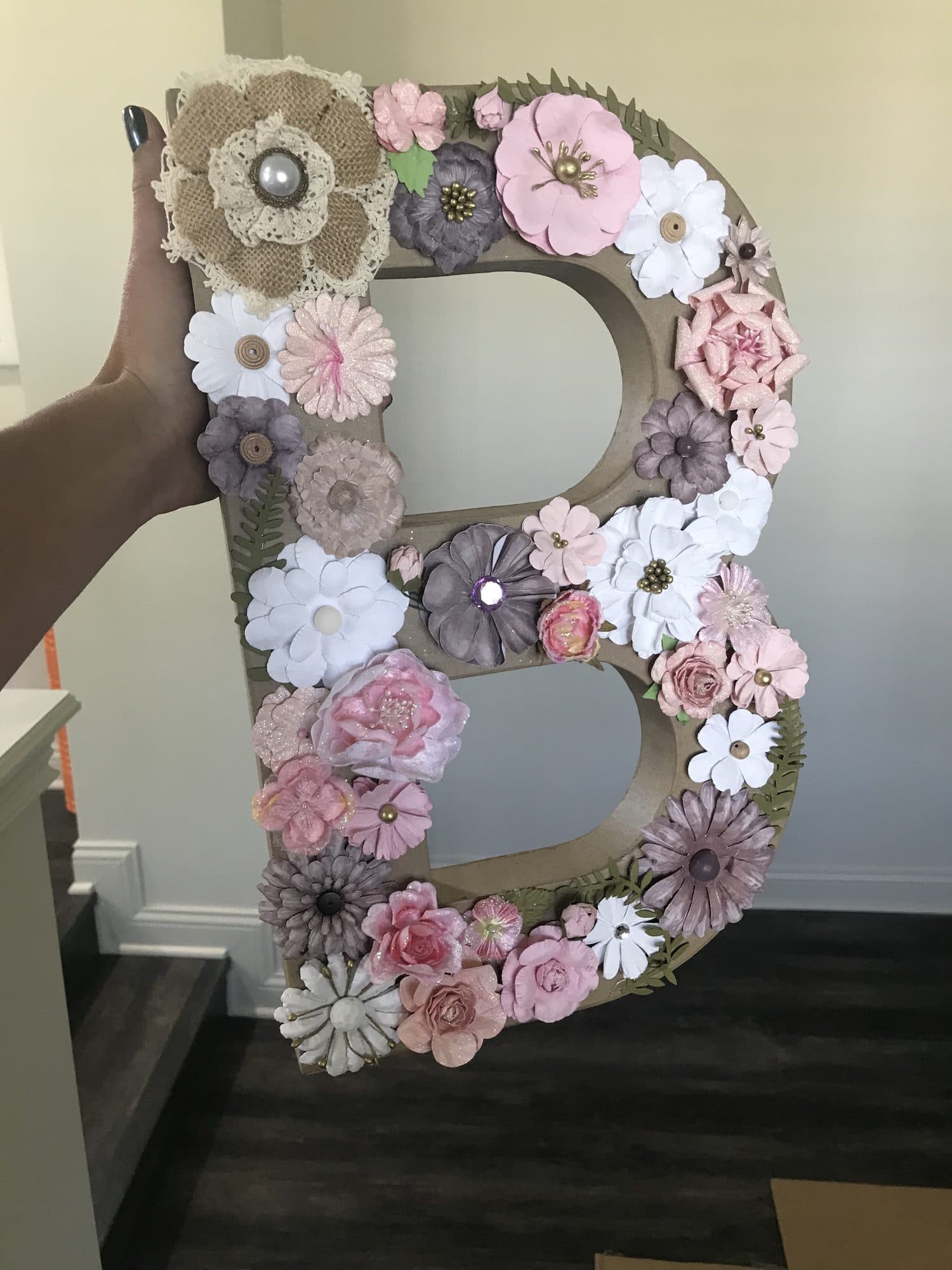 An oversized letter monogram hand-built from blush, mauve, and white paper flowers with burlap-and-lace accents.