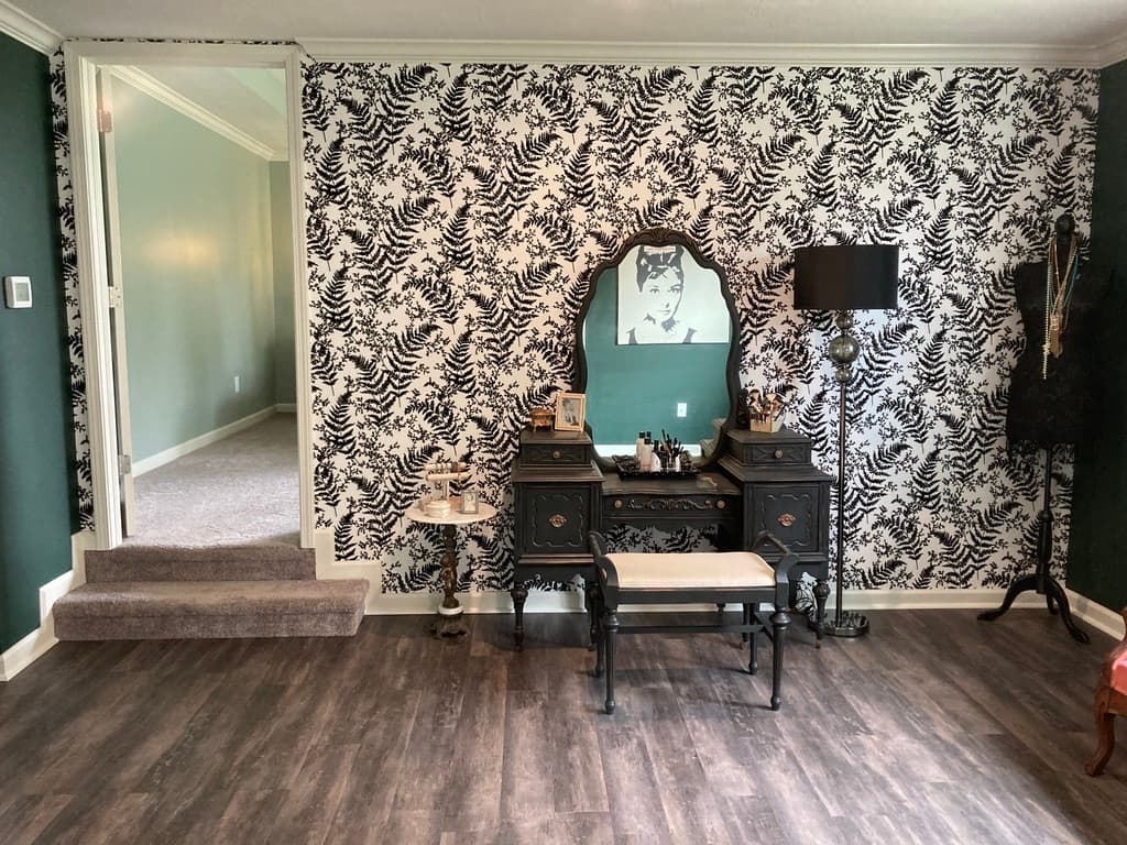 A black-and-white botanical fern wall treatment wrapping a vanity vignette with an arched mirror, vintage dressing table, and Audrey Hepburn print.