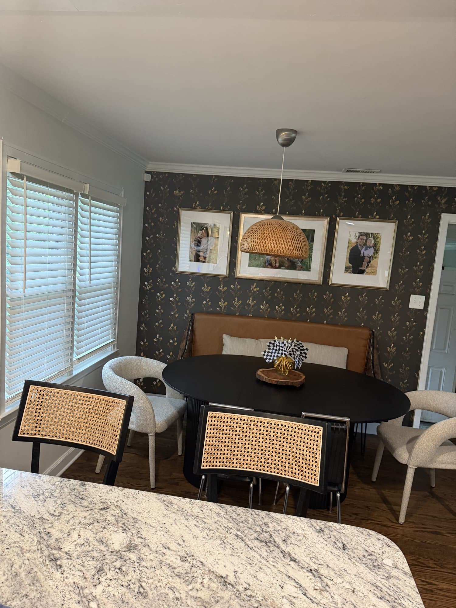 The framed gallery wall arranged across the botanical wallpaper beside the dining table.