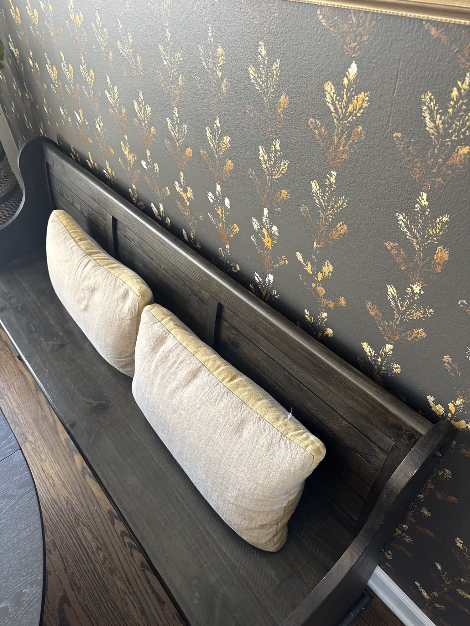 Close detail of the charcoal wallpaper, gold botanical sprays over a deep matte ground, with a bench cushion below.