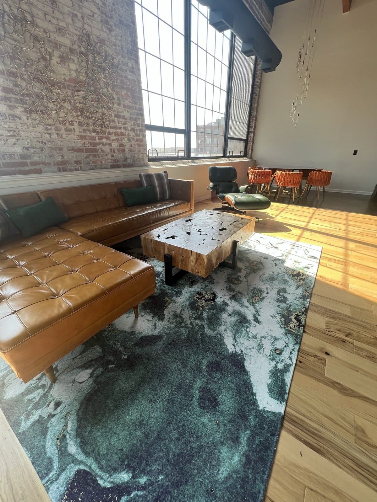 The main living room: a cognac leather sectional on an ocean-swirl rug under tall arched windows and exposed brick.