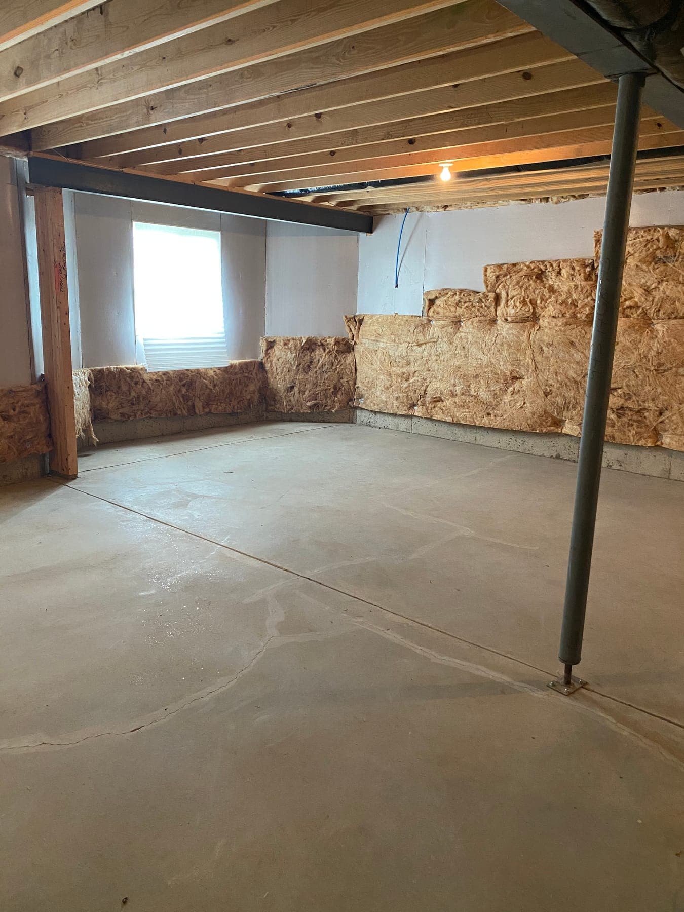 Before, an empty unfinished basement: bare concrete floor, a steel support post, and a raw foundation wall.