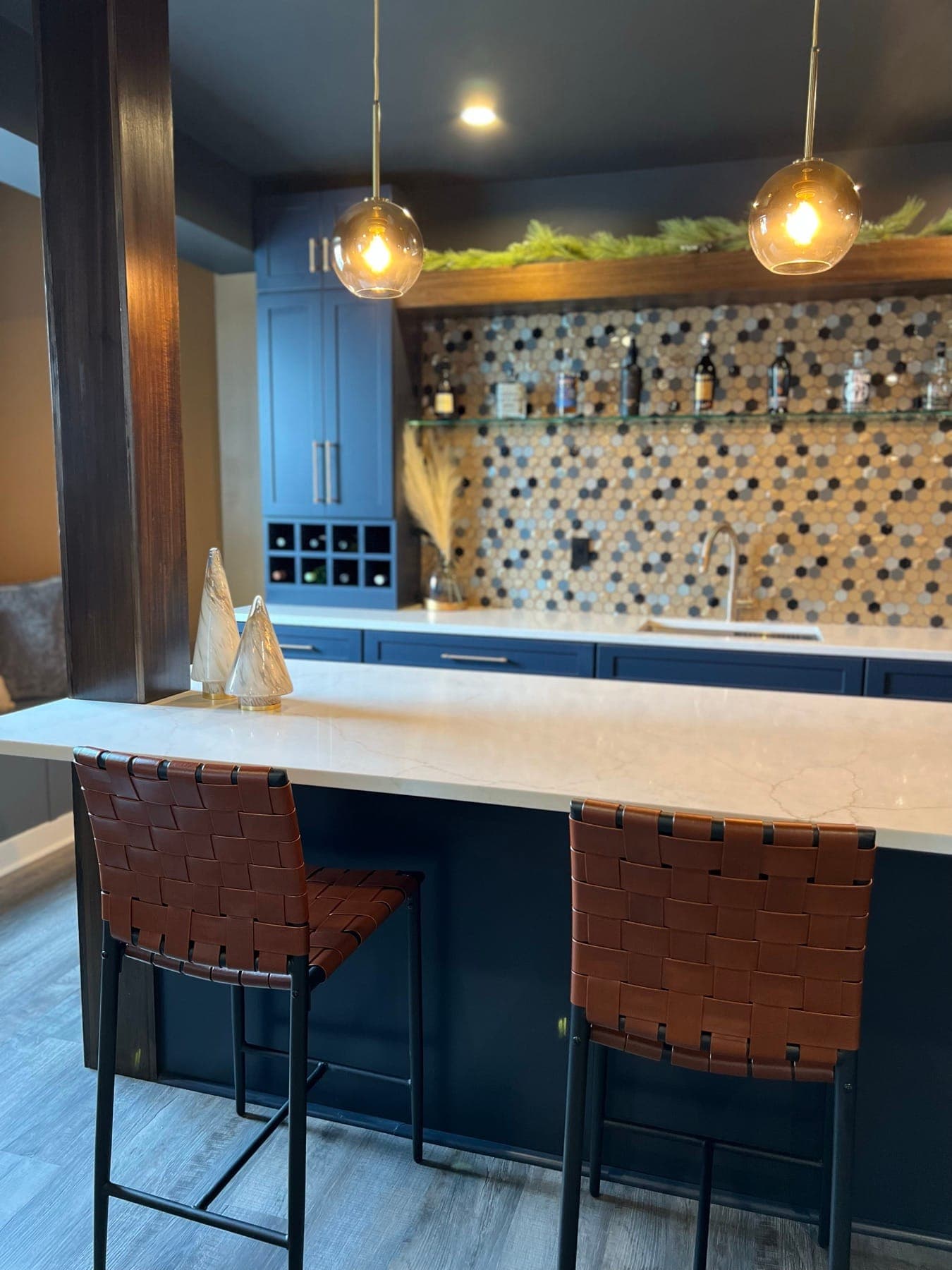 The bar head-on, walnut columns framing the hex-tile wall, brass pendants, and woven leather stools at the quartz counter.