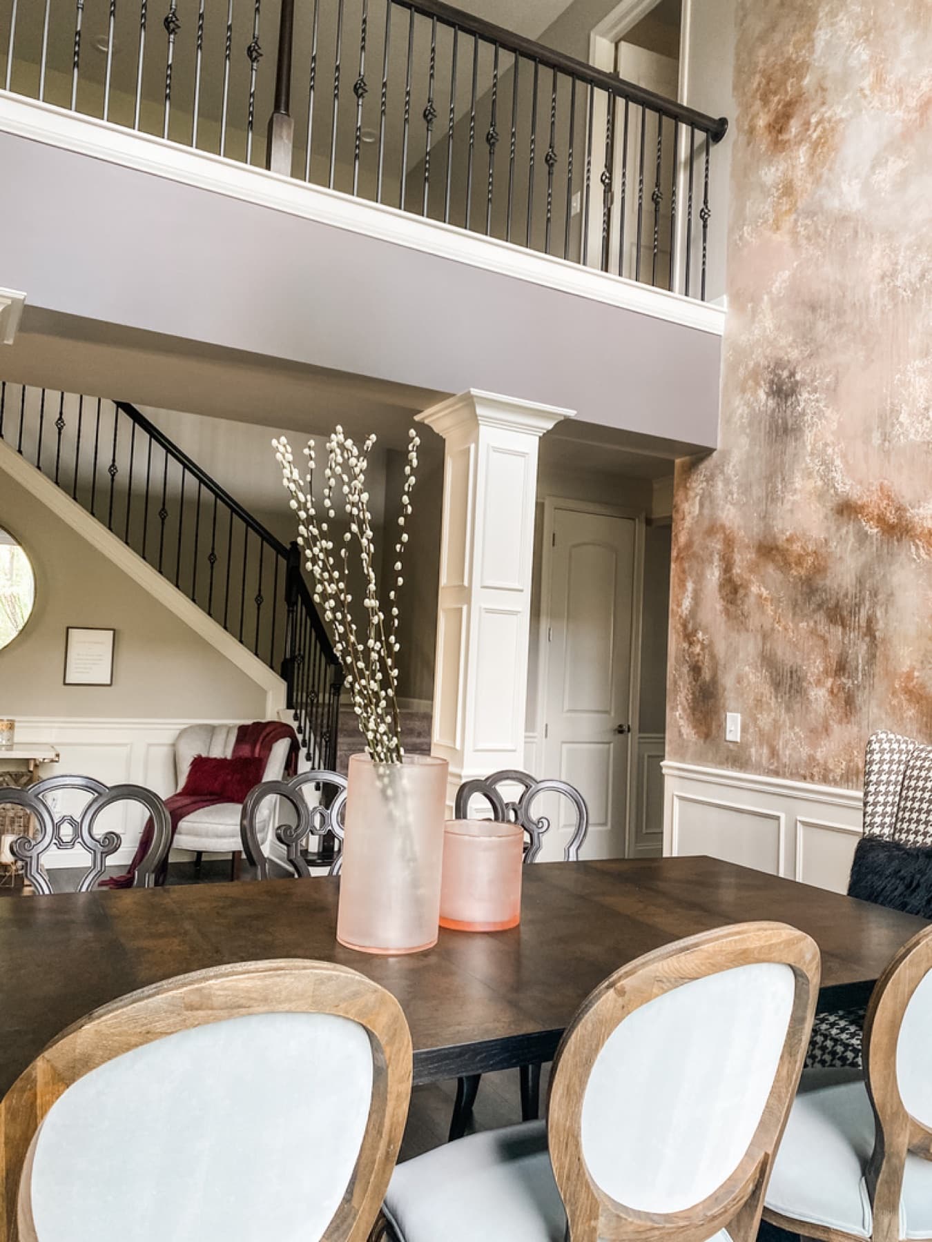 A two-story dining room with a hand-finished copper plaster feature wall, dark wood table, and round-back upholstered chairs.