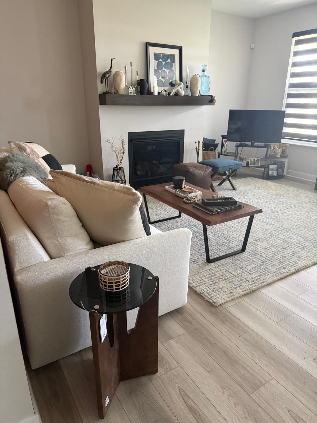 The fireplace side of the living room: a white sofa, a walnut-and-black coffee table, a floating mantel styled with art and ceramics, and a black side table.