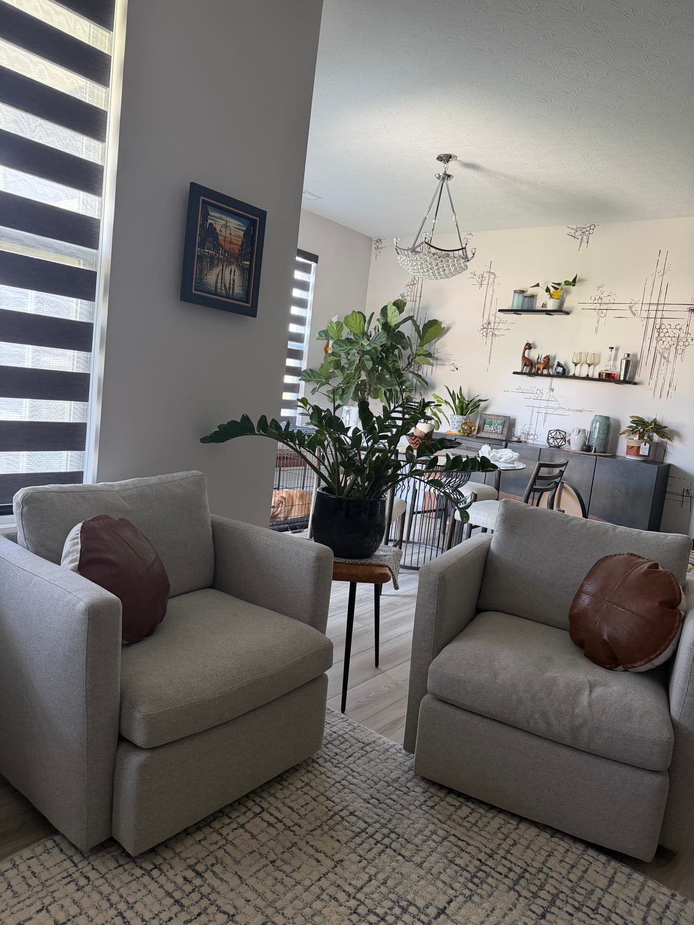 Two gray armchairs with cognac pillows by the window, a small black side table between them, the dining mural beyond.