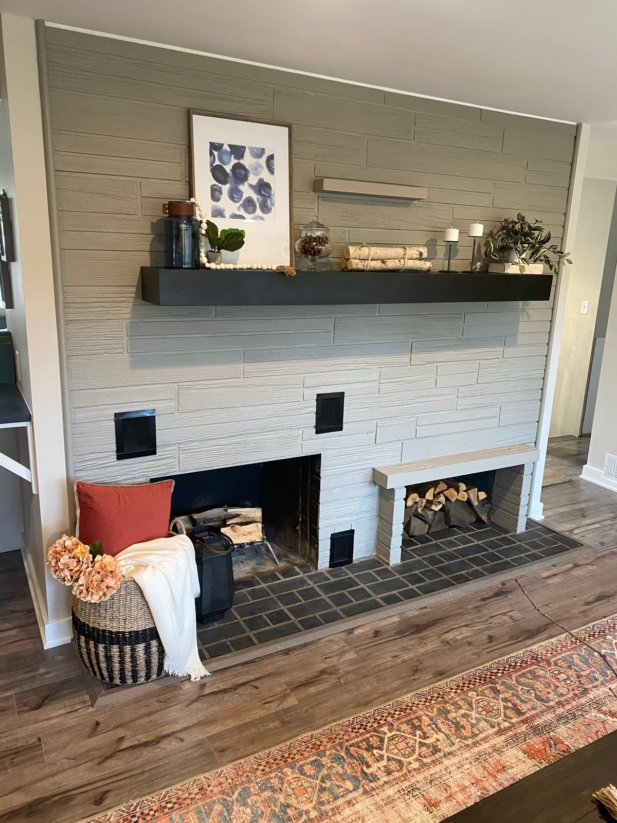 White-shiplap fireplace with a black floating mantel, styled with an abstract print and a rust throw-pillow basket.