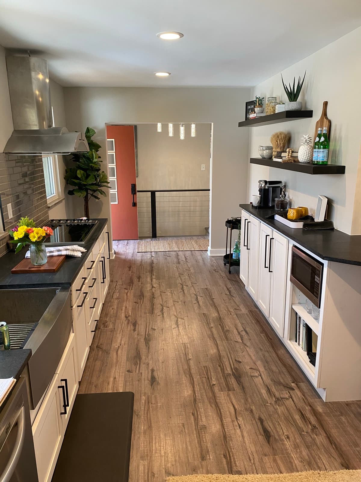 Modern galley kitchen, white shaker cabinets, black countertops, stainless hood, and open shelf styling.