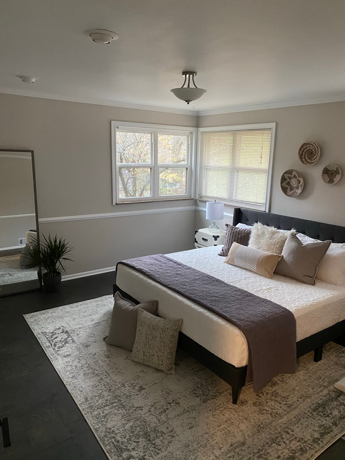 Primary bedroom, upholstered bed dressed in layered neutrals with woven wall baskets and a leaning mirror.