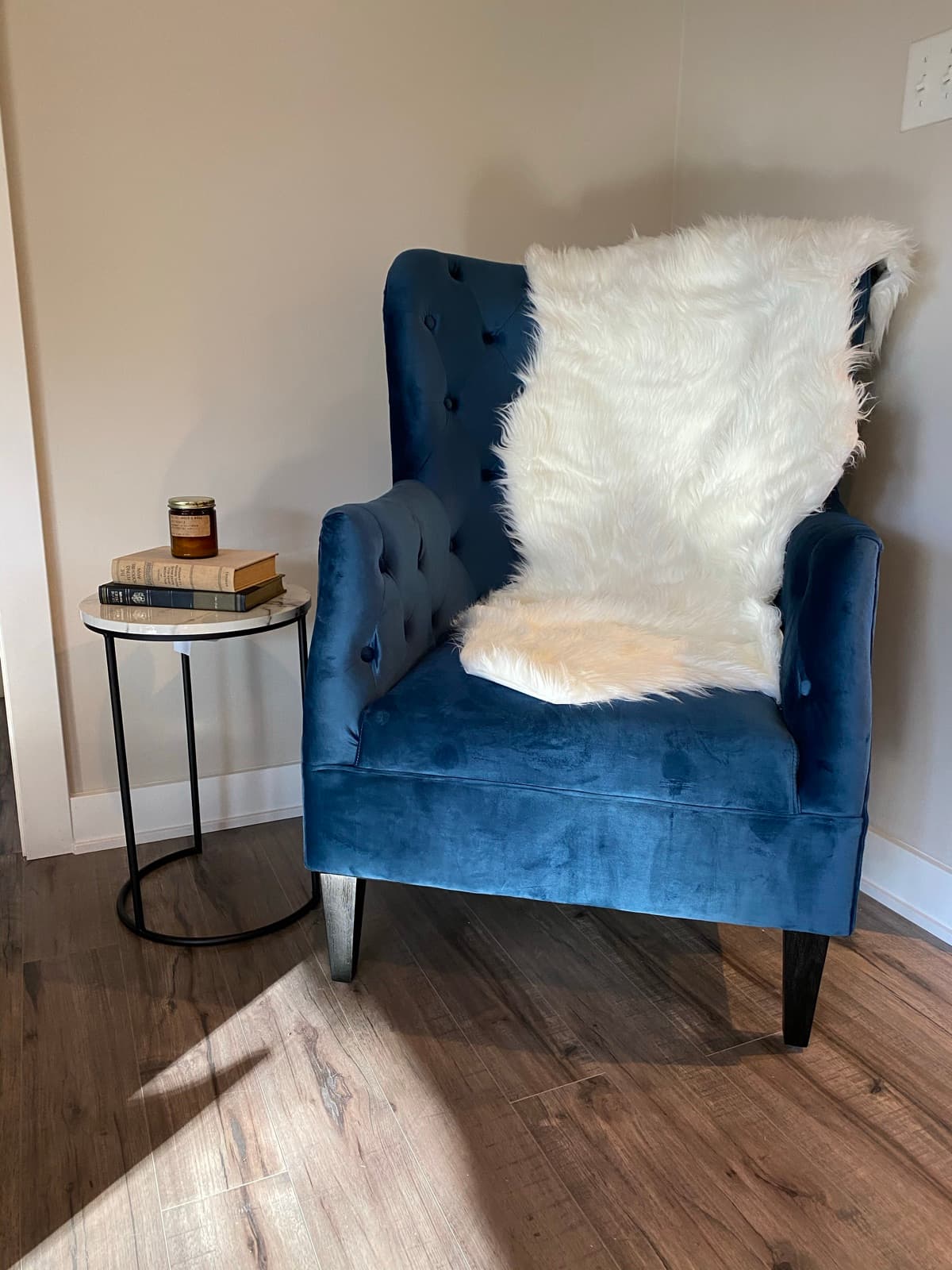 Reading corner, navy velvet tufted wingback with a faux-fur throw and a marble side table stacked with books.
