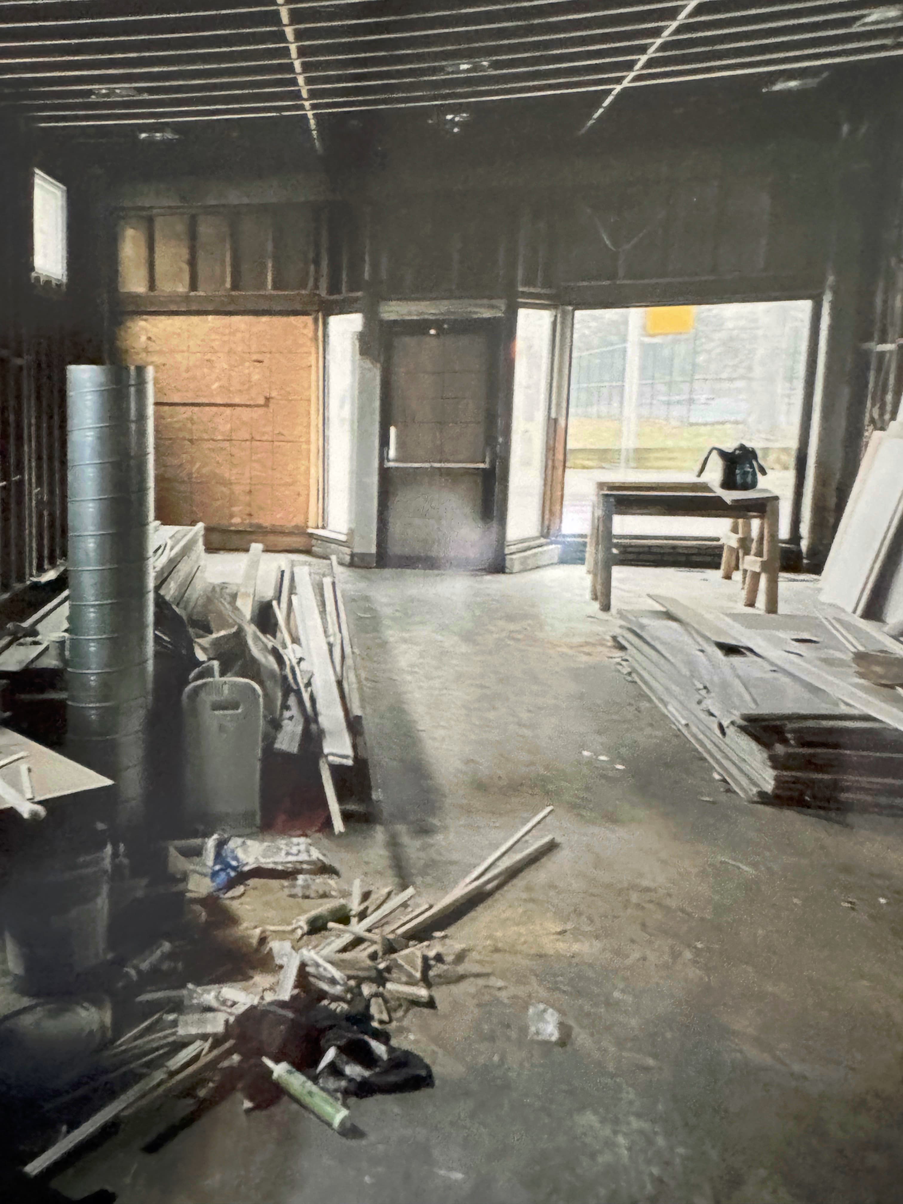 Gutted Indianapolis storefront mid-demolition, exposed framing, construction debris and lumber scattered across the concrete floor.