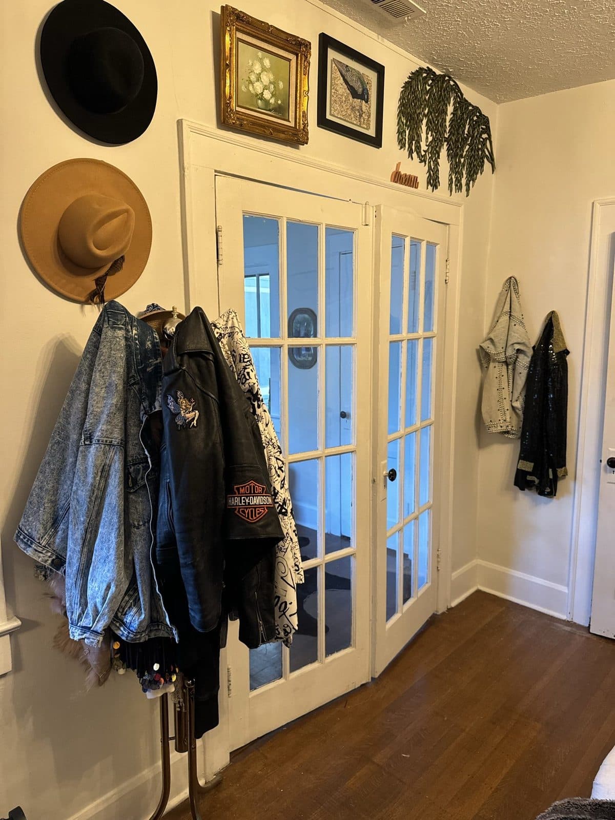 An entry wall of hooks holding hats, denim, and leather jackets beside French doors.