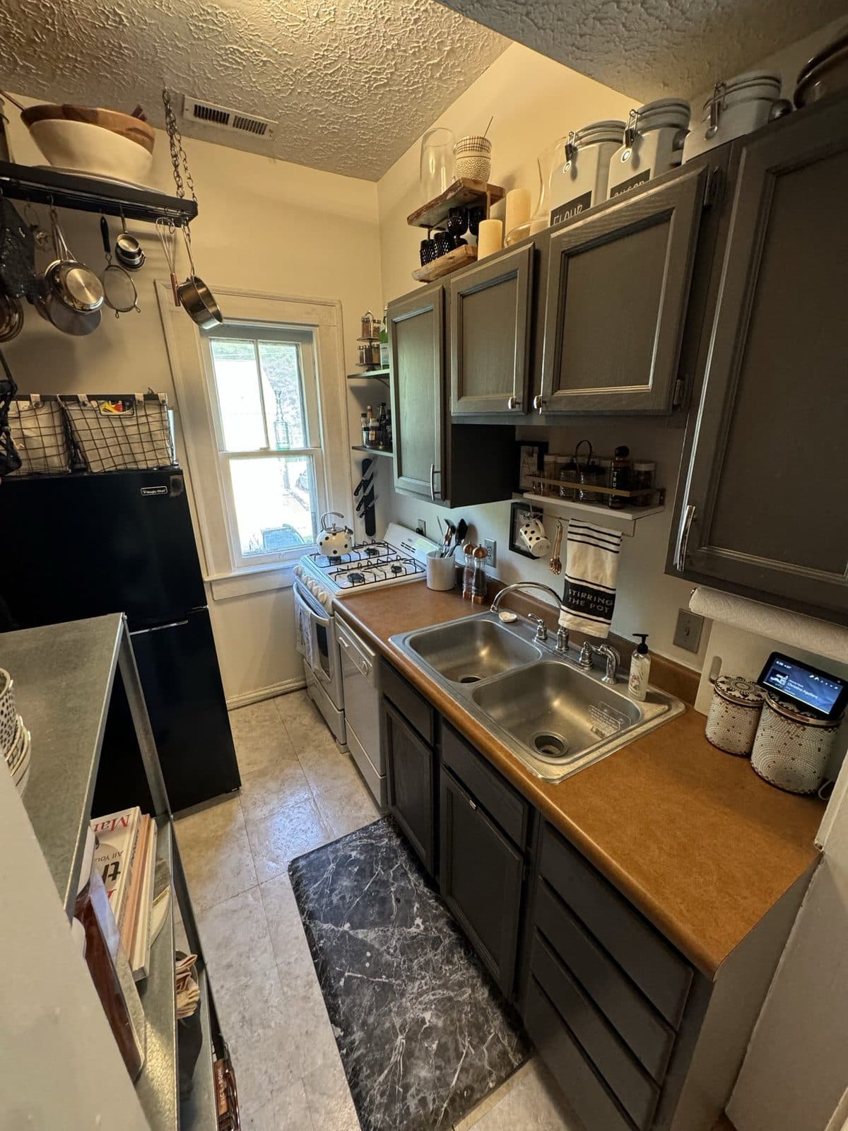 The galley kitchen: charcoal cabinets, a pot rack over the window, and a rolling shelf beside the fridge.