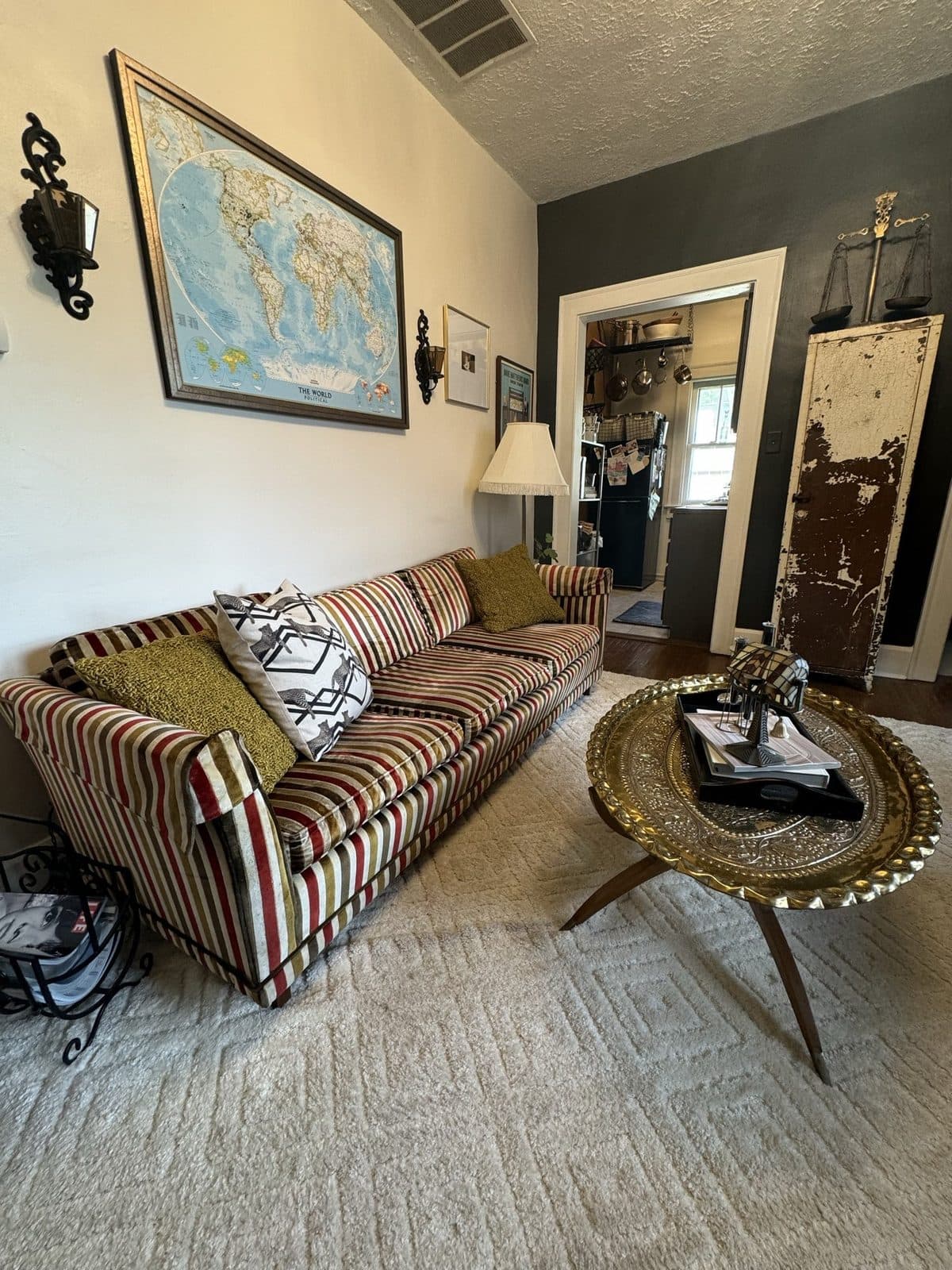 The living room: a striped vintage sofa, a hammered brass coffee table on a jute rug, a large map on the wall.