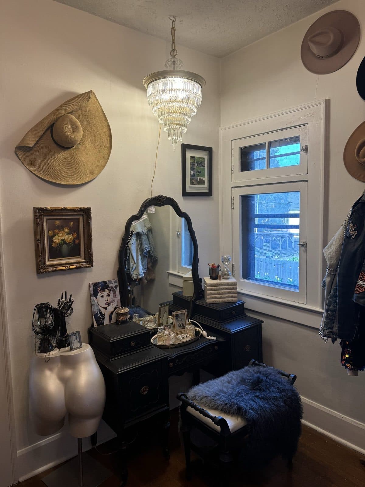 A vanity corner: a black dresser, an ornate mirror, and a wall of straw and felt hats under a ribbed glass pendant.