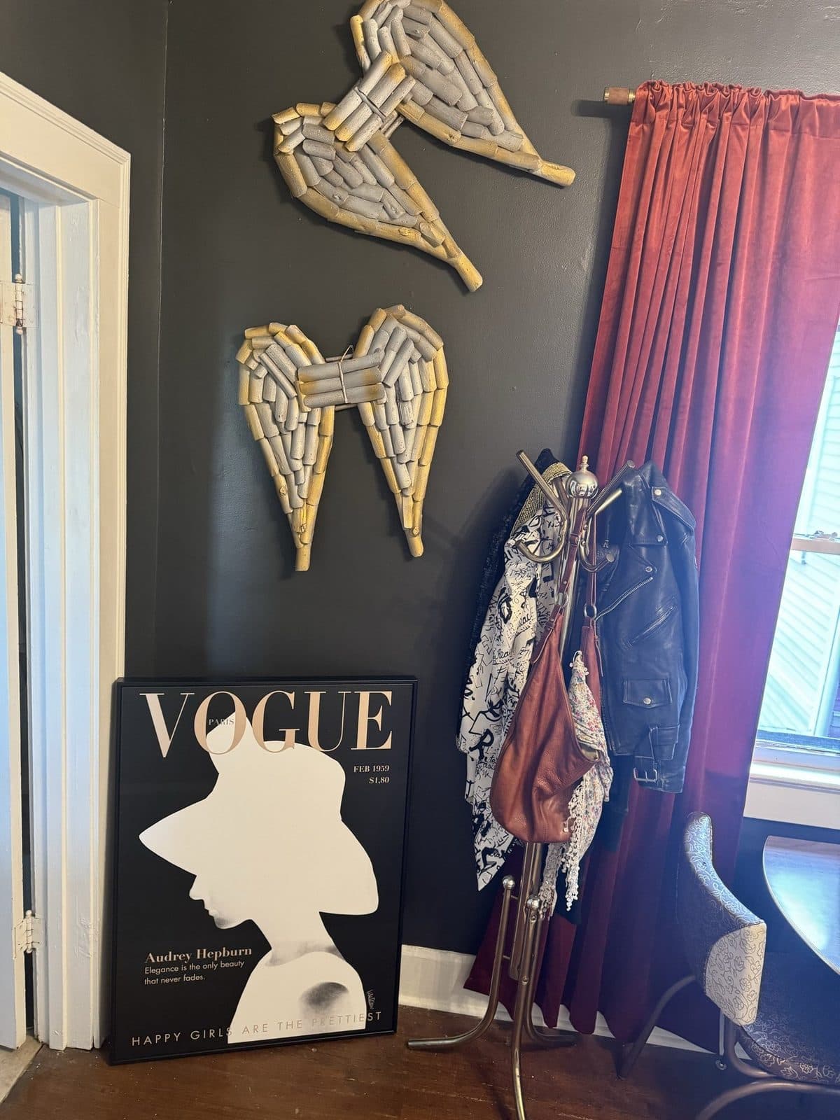 A charcoal accent wall with gilded angel wings, a Vogue print, and a rust curtain beside a salvaged chippy door.
