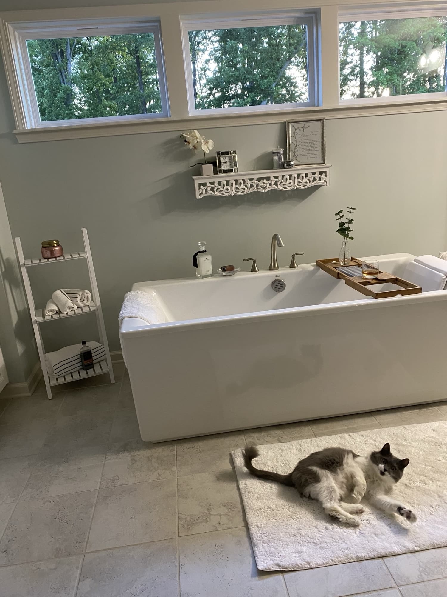The same bath in evening light, greener trees through the windows, a glass resting on the bath caddy.